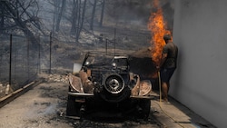 Ein Bewohner versucht, die Flammen im Hof seines Hauses auf Rhodos zu löschen. (Bild: The Associated Press)