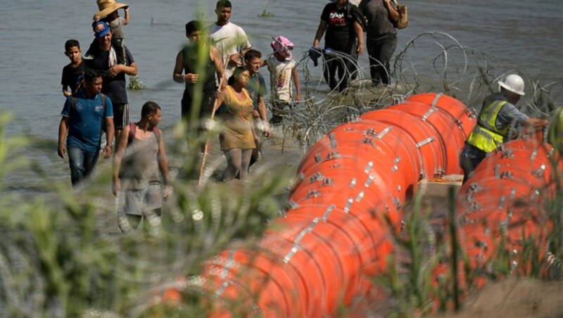 Migranten sehen bei den Errichtungsarbeiten zu. (Bild: AP)