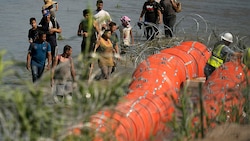 Migranten sehen bei den Errichtungsarbeiten zu. (Bild: AP)