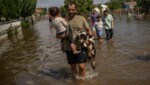 Ein Mann trägt ein Mädchen und einen Hund durch das Hochwassergebiet. (Bild: AFP)