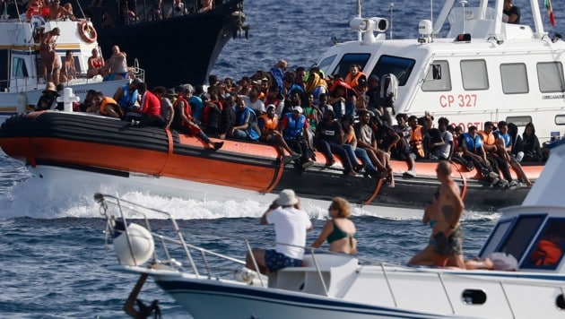 Wenn Welten aufeinander prallen: Touristen beobachten die Ankunft von Migranten vor Sizilien. (Bild: LaPresse)