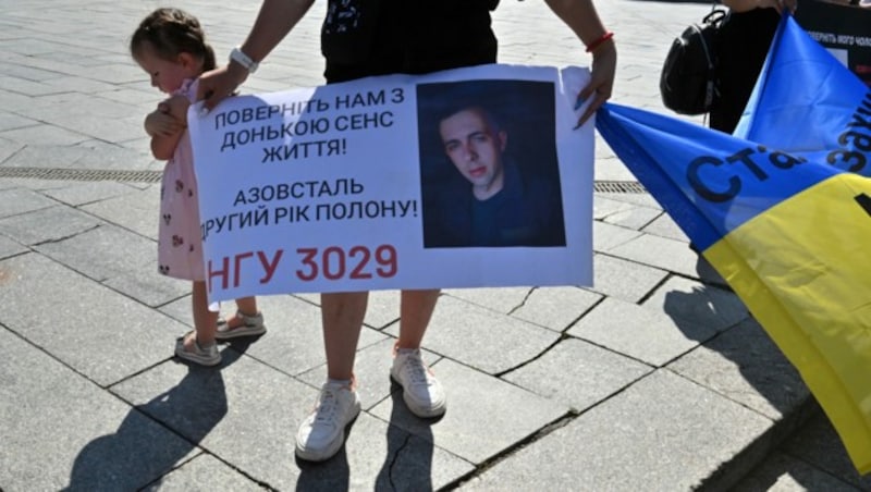 Eine Frau hält in Kiew bei einer Kundgebung ein Plakat mit der Aufschrift „Gebt unserer Tochter den Grund zum Leben zurück“. Darauf zu sehen: das Bild eines ukrainischen Soldaten, wohl der Vater des Kindes. (Bild: AFP)