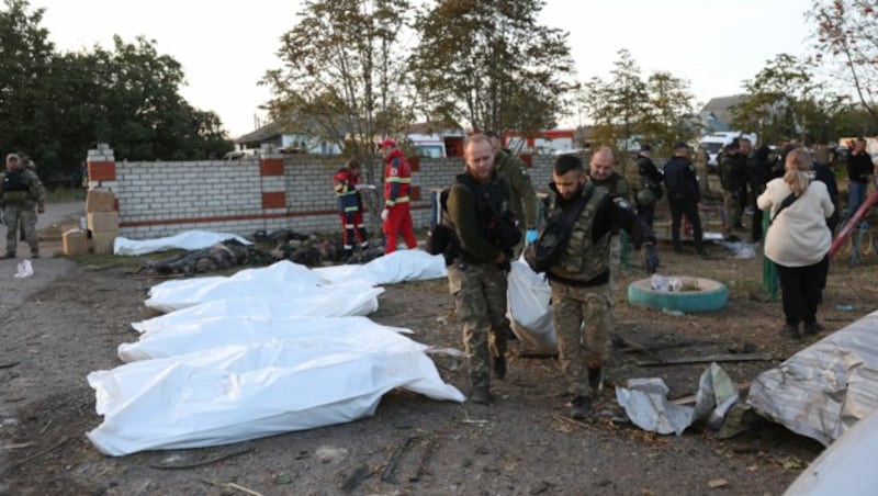 Ukrainische Polizisten tragen nach dem russischen Angriff im Dorf Groza, das etwa 30 Kilometer westlich von Kupjansk in der Ostukraine liegt, Leichen aus dem zerstörten Geschäft und Café. (Bild: APA/AFP/Anatolii STEPANOV)