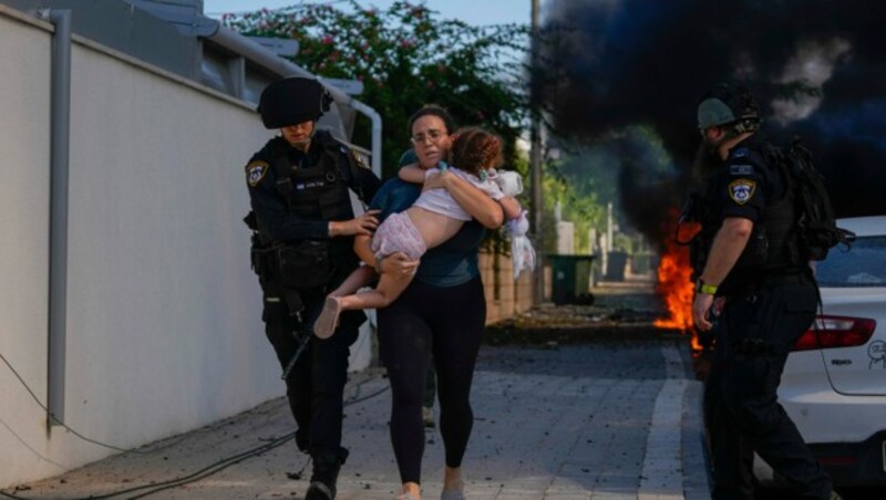 Israelische Polizisten evakuieren eine Frau und ein Kind von einem Ort in Aschkelon im Süden Israels, der von einer aus dem Gazastreifen abgefeuerten Rakete getroffen wurde. (Bild: APA/AP Photo/Tsafrir Abayov)