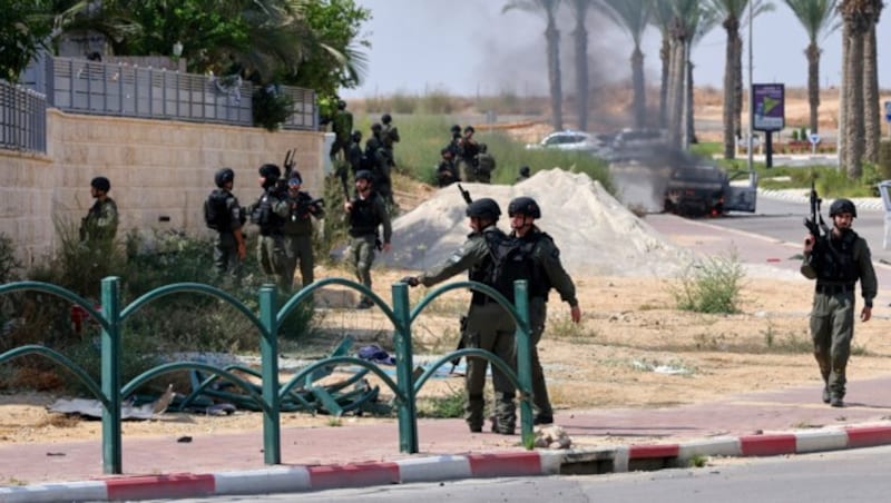 Israelische Soldaten am Sonntag in Ofakim - das brennende Auto im Hintergrund wurde von bewaffneten Palästinensern genutzt. (Bild: AP)