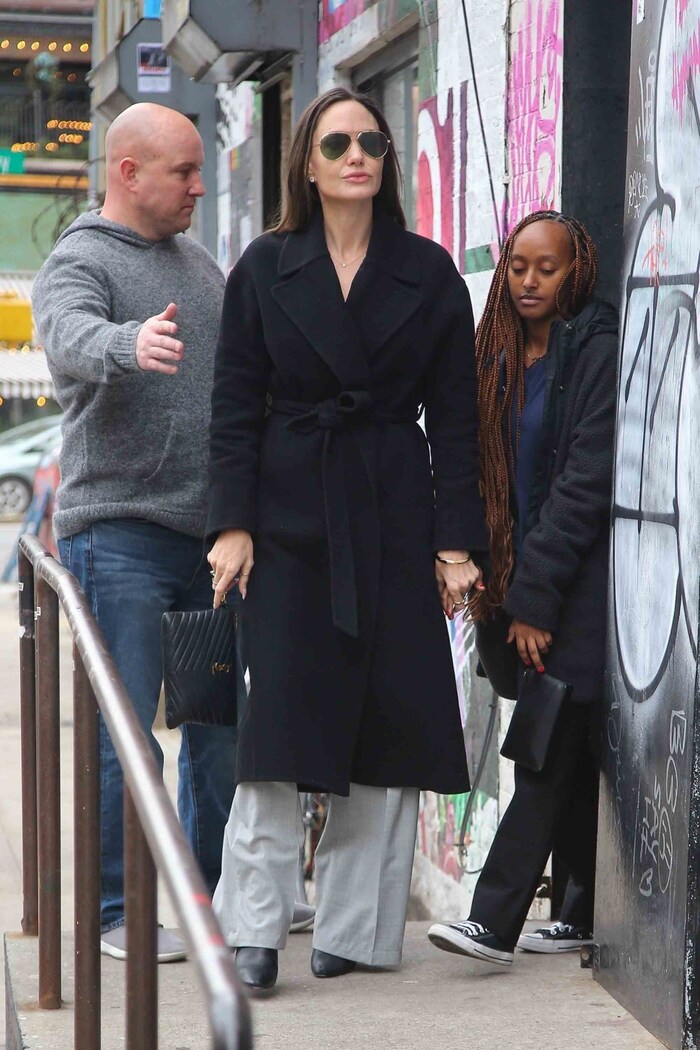 Angelina Jolie kombiniert eine graue Leinenhose. mit einem schwarzen Mantel.