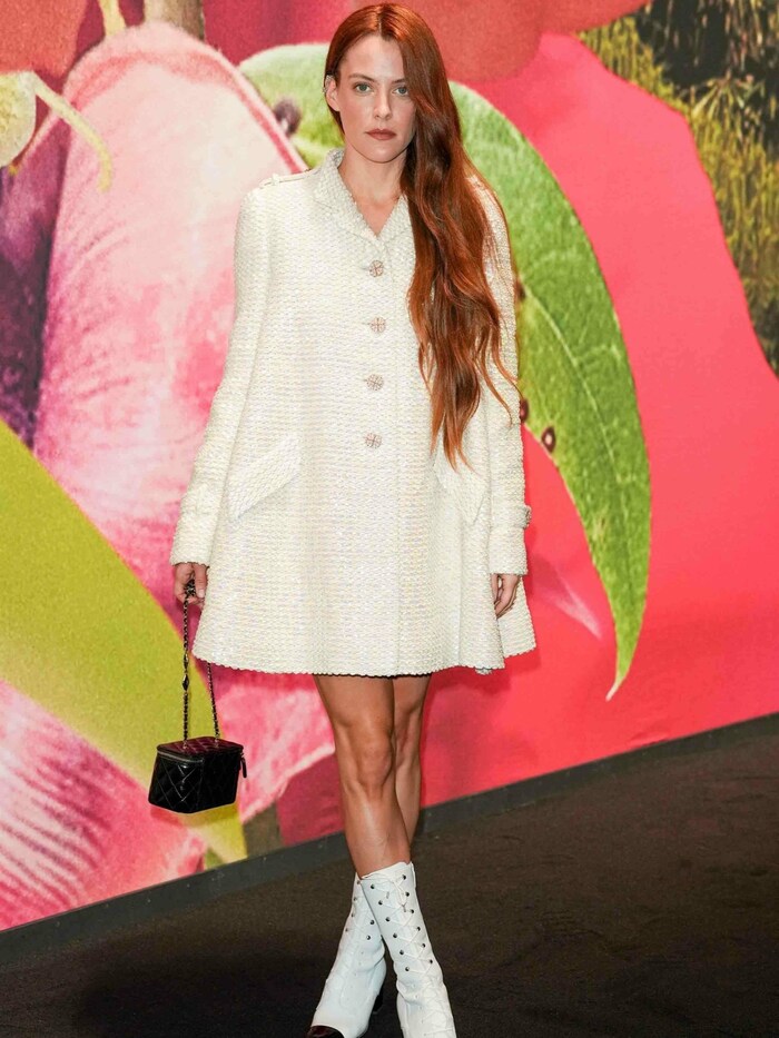 Riley Keough in einem weißen Mantelkleid mit passenden Stiefeletten