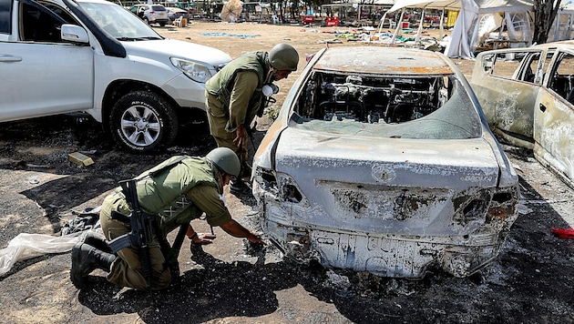 Forensiker der israelischen Armee bei ausgebrannten Wracks am Festivalgelände (Bild: APA/AFP/JACK GUEZ)