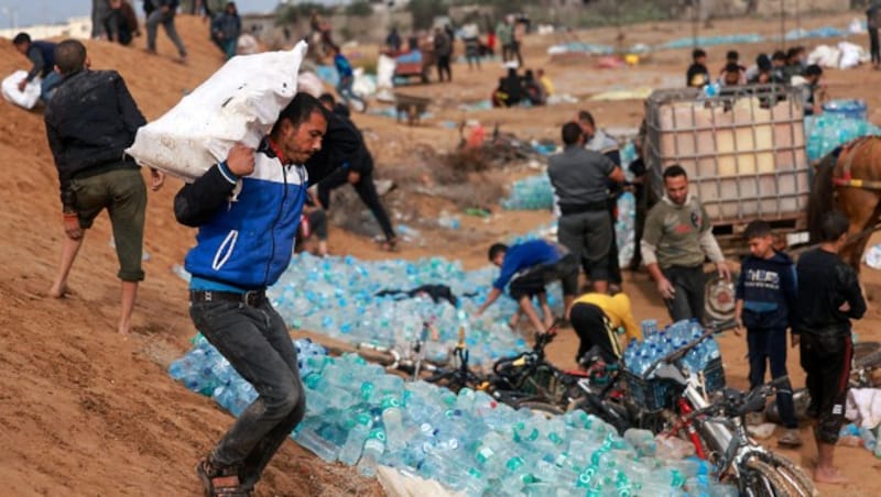 Palästinenser sammeln über den Grenzübergang Rafah gelieferte Wasserflaschen auf. (Bild: APA/AFP/MOHAMMED ABED)