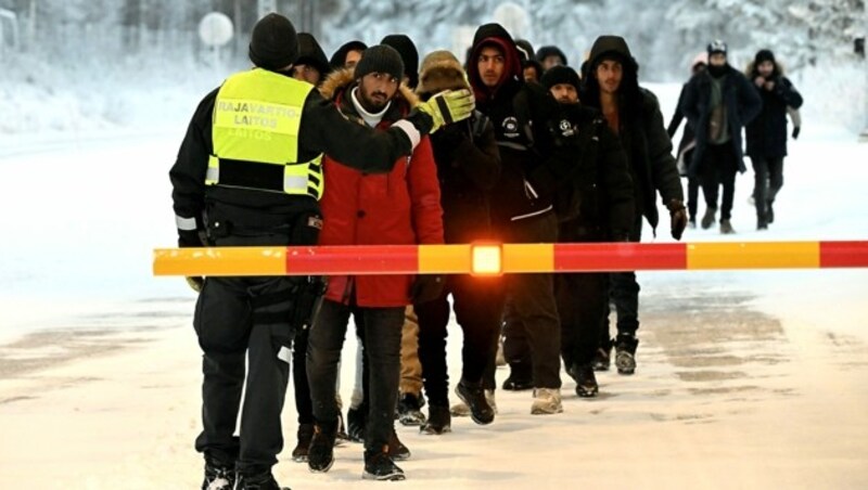 Ein finnischer Grenzwächter eskortiert eine Gruppe von Migranten. (Bild: APA/AFP/Lehtikuva/Jussi Nukari)