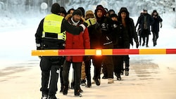 Ein finnischer Grenzwächter eskortiert eine Gruppe von Migranten. (Bild: APA/AFP/Lehtikuva/Jussi Nukari)