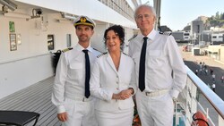 „Das Traumschiff - Walvis Bay": An Deck des Schiffs, das im Hafen ankert, steht Hanna Liebhold (Barbara Wussow) lachend zwischen Kapitän Max Parger (Florian Silbereisen) und Oskar Schifferle (Harald Schmidt). (Bild: ZDF/Dirk Bartling.)
