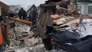 Dieses von der ukrainischen Staatsanwaltschaft veröffentlichte Handout-Foto zeigt Menschen, die auf den Trümmern eines zerstörten Hauses nach russischem Beschuss in Seredyna-Buda in der Region Sumy stehen. (Bild: AFP)
