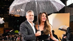George Clooney hält Gentleman-like den Regenschirm für seine Ehefrau Amal. (Bild: Alberto Pezzali/Invision/AP)