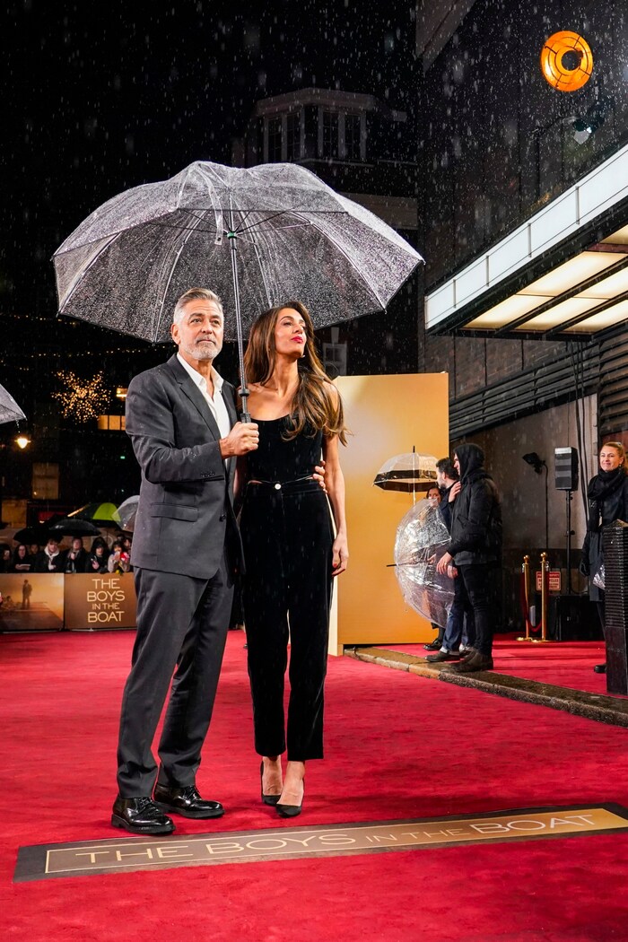Clooney hält den Regenschirm, um seine Frau vor dem Regenguss zu schützen.