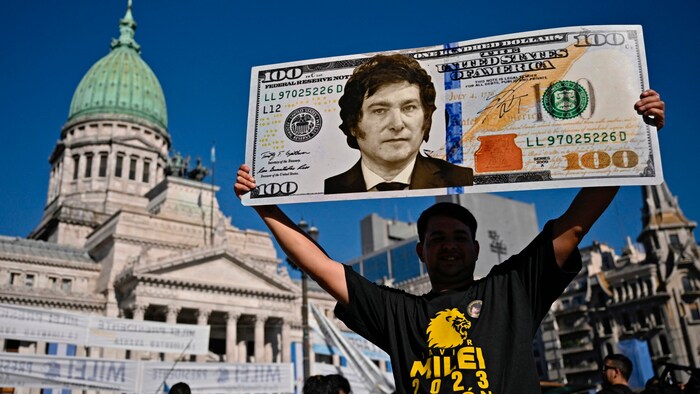 Ein Unterstützer Mileis hält ein Plakat in Gestalt eines 100-Dollar-Scheines mit dem Porträt des ...