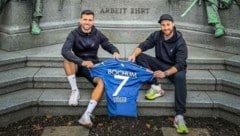 Kevin Stöger (li.) mit Personal Coach Björn Schulz vor dem Werndl-Denkmal in Steyr. Die Aufschrift Arbeit ehrt passt auch zu dem Duo. (Bild: Zur Verfügung gestellt)