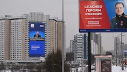 Die Jahreskonferenz des russischen Präsidenten Wladimir Putin wird an einer Häuserfassade übertragen. Rechts davon wird ein russischer Soldat auf einem Plakat geehrt. (Bild: APA/AFP/NATALIA KOLESNIKOVA)