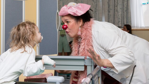 Schon Verkleidung, Clown-Nase und Name sorgen für ein Lachen: „Dr. Prof. Lotte Ledig“ besucht eine kleine Patientin, die eine Aufmunterung brauchen kann.  (Bild: CliniClowns Austria/Christoph Schiele)