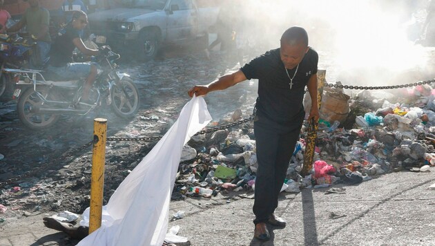Un homme soulève un drap à Pétion-Ville pour identifier un mort en dessous. (Bild: Associated Press., Krone KREATIV)