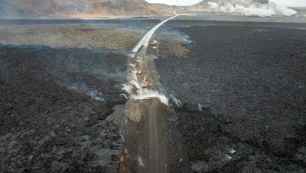 Perşembe günü inşaat işçileri, kalın bir çakıl tabakasıyla kaplı olan ve hala sıcak olan lavların üzerine yeni bir yol inşa etmeye başladı. (Bild: x.com (Screenshot))