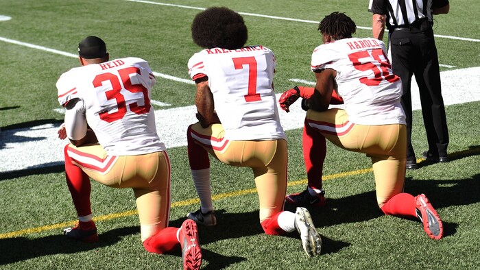 Colin Kaepernick (m.) kneels during the US anthem.