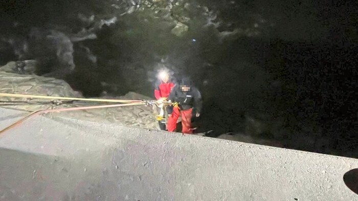 The mountain rescuers pulled the fallen man out of the stream bed up to the road using a rope.