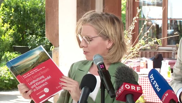 Klimaschutzministerin Leonore Gewessler zeigt den „APCC Special Report Landnutzung und Klimawandel in Österreich“ her. (Bild: APA/Screenshot Livestream)