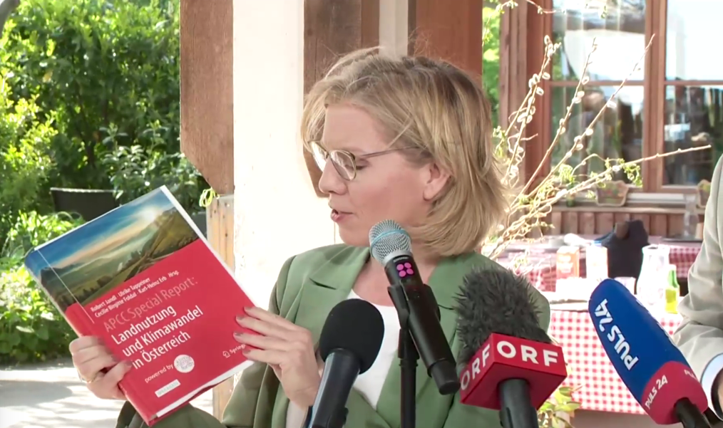 Klimaschutzministerin Leonore Gewessler zeigt den „APCC Special Report Landnutzung und Klimawandel in Österreich“ her. (Bild: APA/Screenshot Livestream)