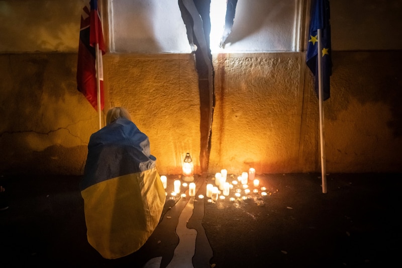 A woman wrapped in a Ukrainian flag lights a candle at the memorial for Ján Kuciak and his fiancée Martina Kušnírová. (Bild: AFP/VLADIMIR SIMICEK)