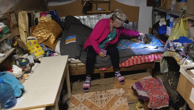 Eine Frau streichelt ihren Hund im Keller eines beschädigten Wohnhauses, am Kopf trägt sie eine ...