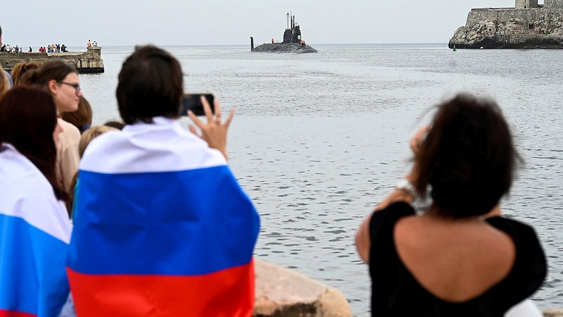 Einige Schaulustige warteten in russische Flaggen gehüllt auf die Ankunft der Kriegsschiffe. (Bild: APA/AFP/YAMIL LAGE)