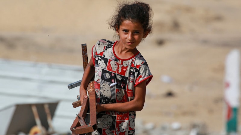 Ein Mädchen trägt Metallteile, während palästinensische Familien ihre Habseligkeiten packen. (Bild: APA/AFP/Bashar TALEB)