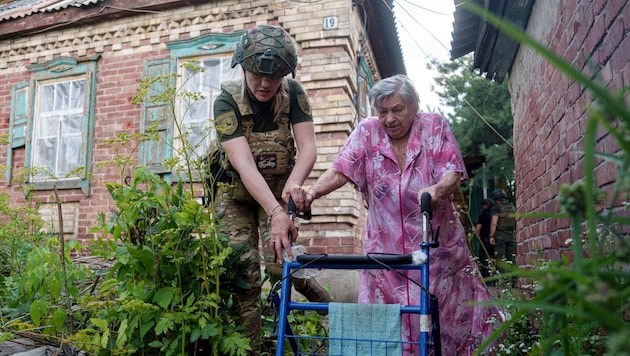 Egy rendőr segít egy ukrán nőnek biztonságosabb környékre jutni. (Bild: AP/Evgeniy Maloletka)