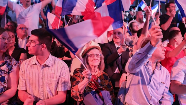 Ok az ünneplésre: Marine Le Pen jobboldali populista pártjának, a RN RN-nek a támogatói francia zászlókat lengetnek az első előrejelzések közzététele után. (Bild: AFP/FRANCOIS LO PRESTI / AFP)