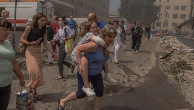 Egy nő biztonságba helyezi gyermekét a becsapódás után. (Bild: AFP/Roman PILIPEY)