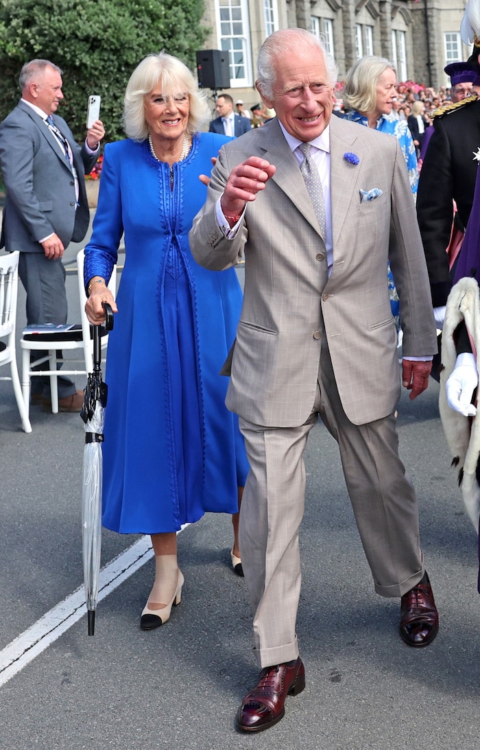 Queen Camilla laughs despite her foot injury on Guernsey. An umbrella serves as additional ...