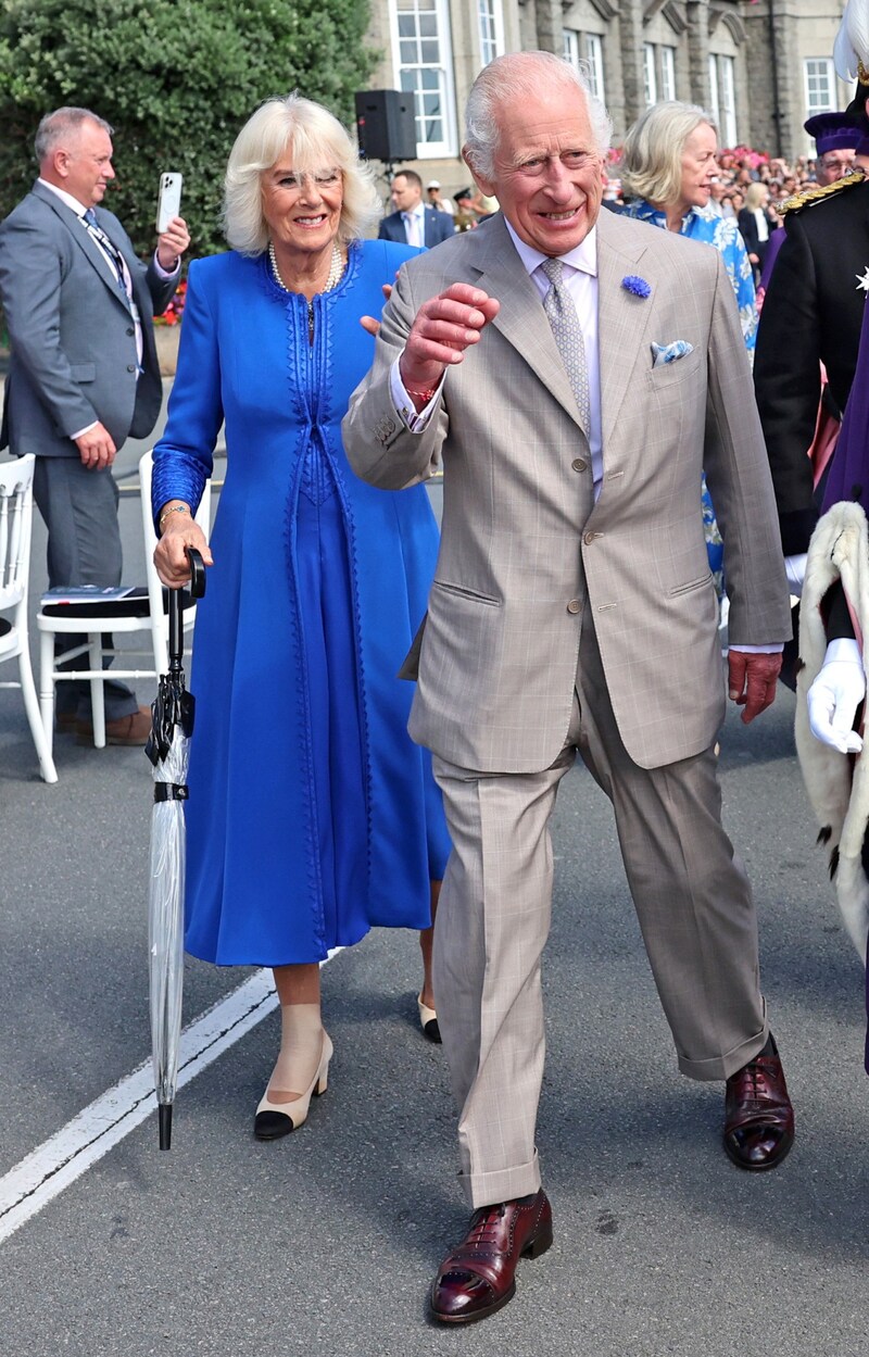 Queen Camilla laughs despite her foot injury on Guernsey. An umbrella serves as additional support. (Bild: picturedesk.com/Chris Jackson / PA)