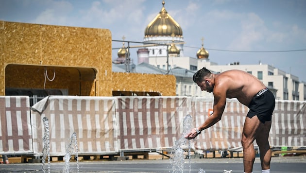 Ein Mann sucht mitten im heißen Moskau nach Abkühlung. Im Hintergrund ist die berühmte Christ-Erlöser-Kathedrale zu sehen. (Bild: APA/AFP/Alexander NEMENOV)