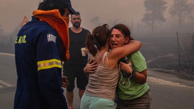 Frauen umarmen sich, nachdem sie bei einem Waldbrand in Varnavas, nördlich von Athen, gerettet wurden. (Bild: APA/AFP/Angelos TZORTZINIS)