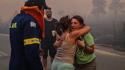 Frauen umarmen sich, nachdem sie bei einem Waldbrand in Varnavas, nördlich von Athen, gerettet wurden. (Bild: APA/AFP/Angelos TZORTZINIS)