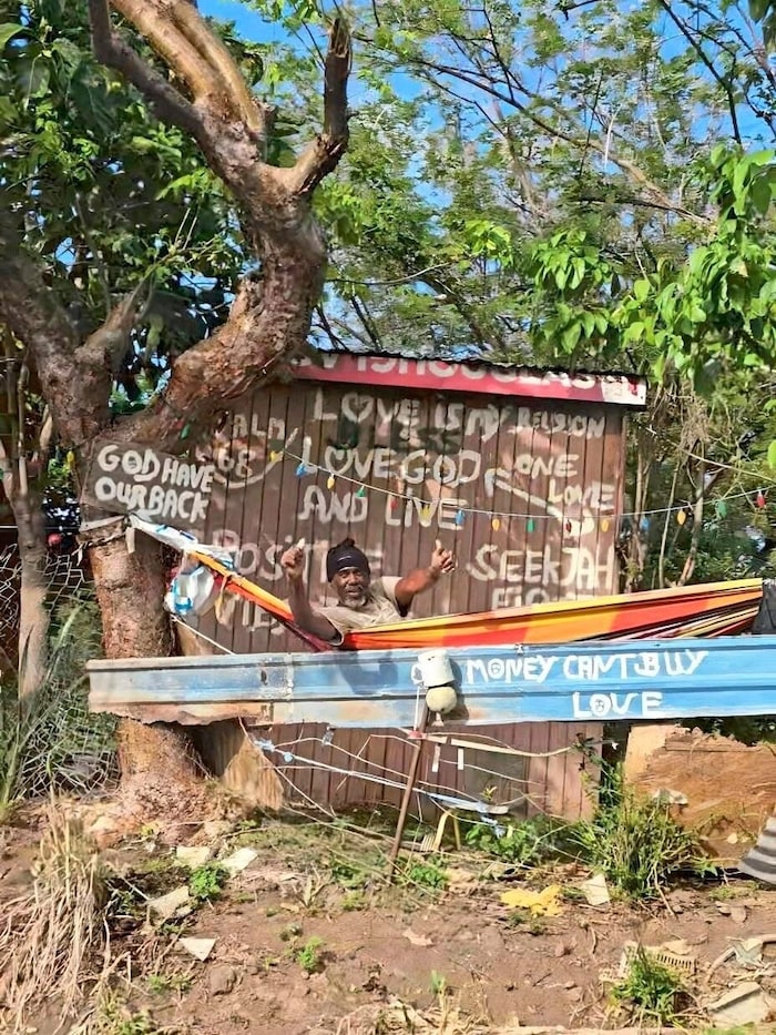 As the train passes, a resident in his hammock waves to the passengers.