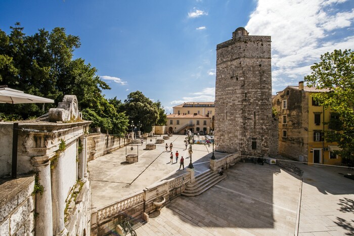 Historic square with five fountains, surrounded by medieval walls.