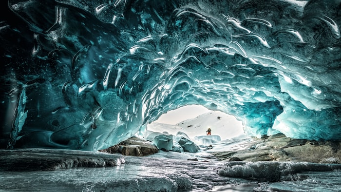 The glacier gate appears as a shimmering blue ice cave and contrasts with the discolored surface, which is covered in rubble and scree.