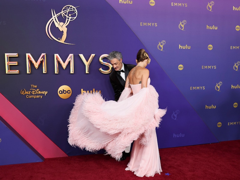 Taika Waititi hilft seiner Frau Rita Ora mit ihrem Kleid. (Bild: AP ( via APA) Austria Presse Agentur/Danny Moloshok/Invision)