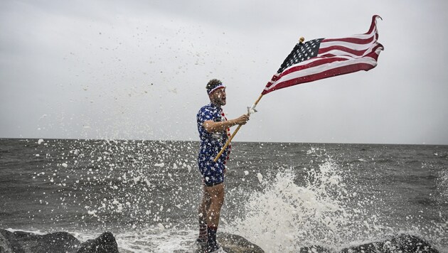 YouTuber Mark Peyton holds up a US flag on the Florida coast shortly before the arrival of "Helene". (Bild: AFP)