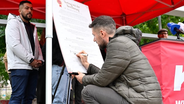 KPÖ top candidate Tobias Schweiger symbolically signs a contract. (Bild: APA/Hans Klaus Techt)