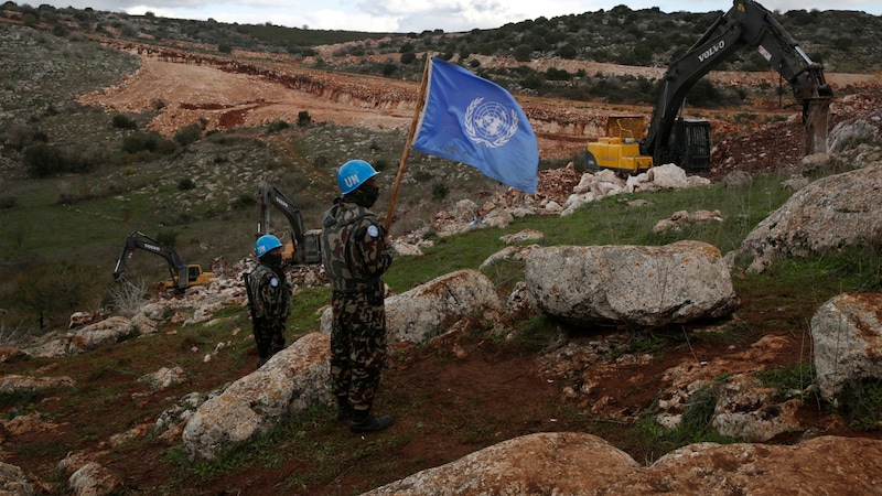 UN peacekeepers hold up their flag as Israeli excavators attempt to destroy tunnels built by Hezbollah near the southern Lebanese-Israeli border village of Mays al-Jabal. (Bild: ASSOCIATED PRESS)