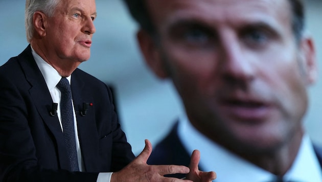 French Prime Minister Michel Barnier speaks next to a screen with a picture of French President Emmanuel Macron during the political television program "L'Evenement" ("The Event"). (Bild: APA Pool/Thomas SAMSON / AFP)