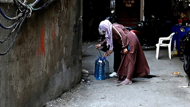 Palestinian refugees in Beirut fill drinking water into the containers they have brought with them. (Bild: APA/AFP/JOSEPH EID)